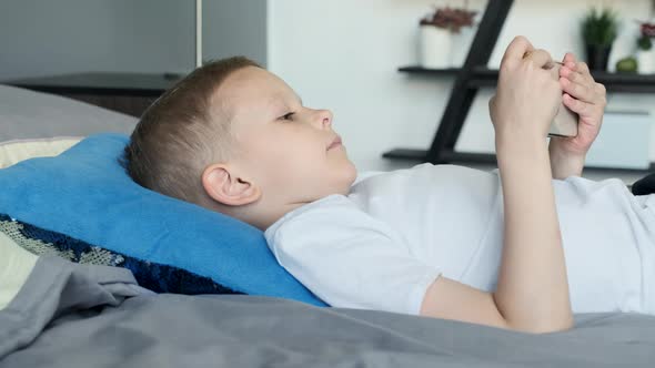 View from the Side A Child Boy Looks at the Phone Screen Plays a Game on A Smartphone alt