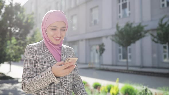 Young Beautiful Muslim Woman Wearing Hijab Headscarf Walking in the City Using Smartphone and