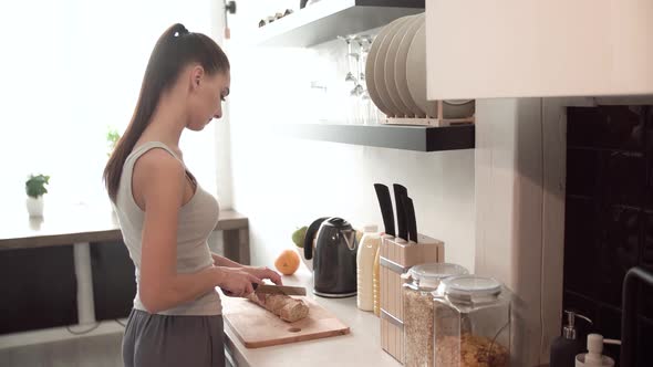 Woman Preparing Breakfast, Cutting Bread On Board In Kitchen alt