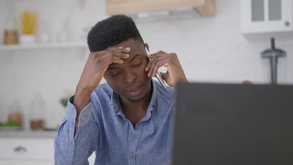 Portrait of Young Professional Man Rubbing Forehead Talking on the Phone in Home Office alt