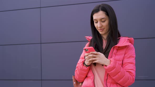 Gorgeous Girl in Pink Texting on Her Smartphone Outdoors alt