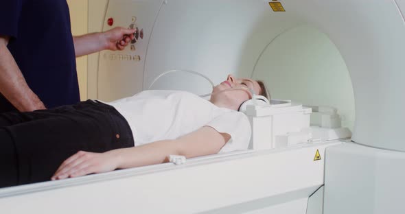 A Patient Wearing Earphones Enters a CT Scan Tunnel for an MRI of the Brain alt