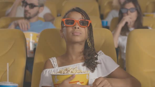 Concentrated African American Girl with Afro Pigtails Sitting with Popcorn in Movie Theater and alt