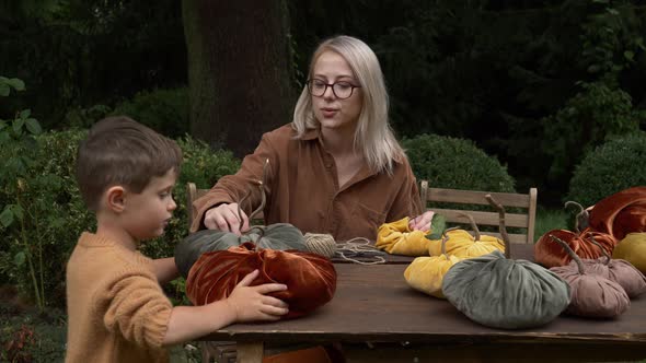 mother with son make pumpkins made of fabric on wooden table in garden