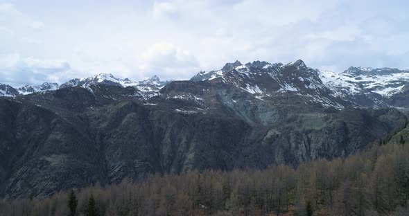Moving Backward Above Clear Blue Lake to Pine Fir or Larch Woods Forest and Snowy Mountain in Autumn alt
