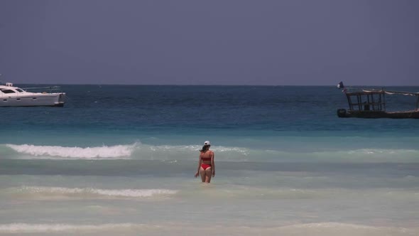 Young Woman in a Red Swimsuit Walks Into the Turquoise Ocean on a Paradise Beach alt