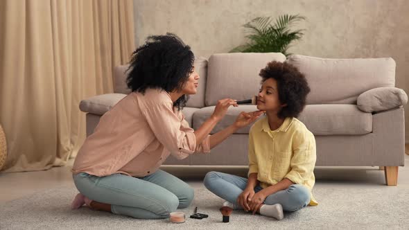 African American Woman Playing with Little Girl Using Makeup Brushes alt