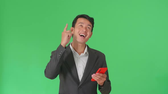 Asian Business Man Use Phone And Thinking Then Raising Her Index Finger In Green Screen Studio alt