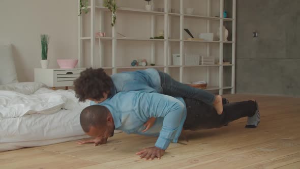 African Man Doing Push-ups with Son on His Back alt