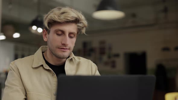 Focused Young Man Sitting at Cafe Table with Laptop