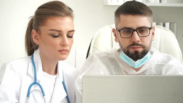Female and Male Doctors Discuss Patients Diagnosis at Laptop in Clinic