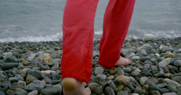 Barefooted Woman Is Stepping Over Large Pebbles on Beach, Moving To Sea Water Line alt