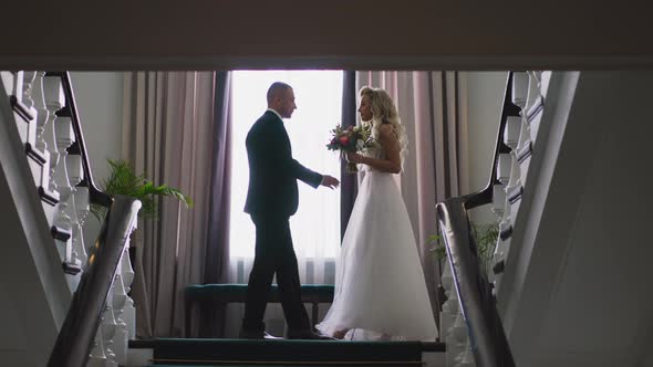 Pretty Bride and Happy Groom Meet Halfway on Staircase alt