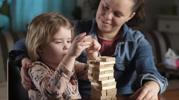 mother with happy little daughter is having fun building tower of wooden blocks alt