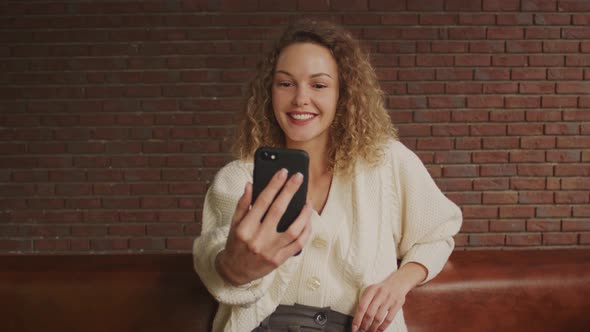 Young Curly Blond Caucasian Woman Chatting on a Video Call with a Smile alt