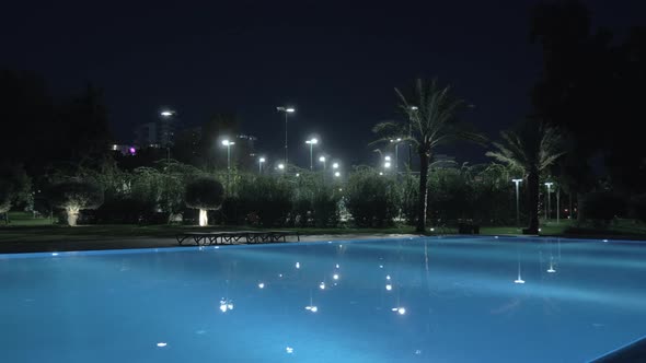 A steadicam shot of an illuminated open pool at night alt