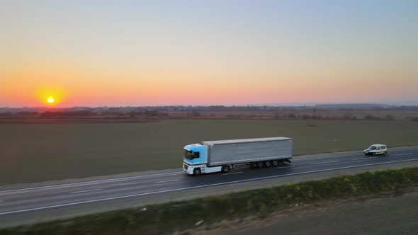 Aerial View of Semitruck with Cargo Trailer Driving on Highway Hauling Goods in Evening alt