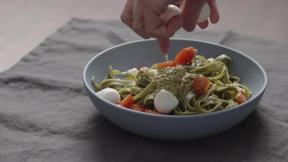 Slow Motion Man Hand Add Mozzarella Balls To Green Fettuccine with Pesto in Blue Bowl alt