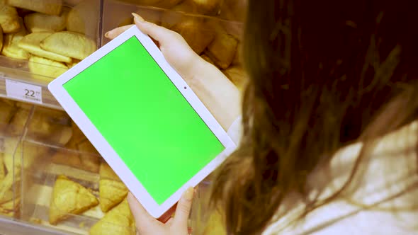 Closeup of a Young Woman's Hand Holding a Tablet Computer with a Green Screen Layout alt