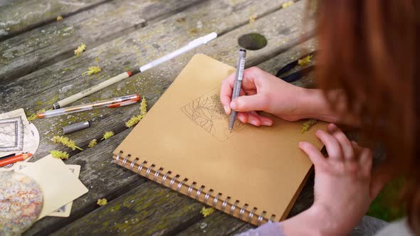 Woman Draws Floral Pattern in Sketchbook Sitting at Table