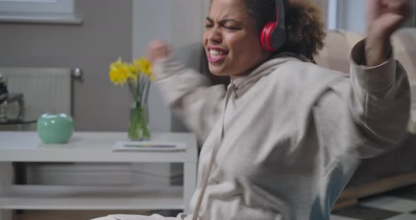 Middle Shot of Joyful African American Woman Enjoying Music in Headphones Dancing Indoors alt