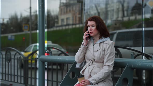 Woman Talking on Phone at Bus Stop in Rainy Weather alt