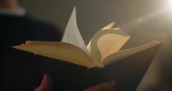 Close-up, the Guy Is Quickly Flipping an Old Book and Dust From It Is Flying Out To the Light. A alt