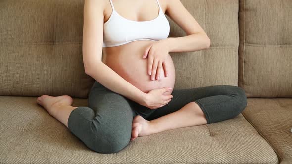 Closeup of the Pregnant Woman Stroking Her Stomach on Sofa alt