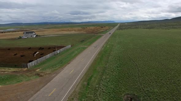 Drone following car on road past farm in flat landscape alt