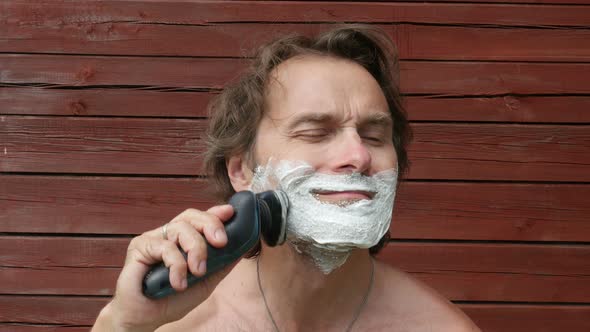 Middle Age Man Shaves His Beard With Foam, Sitting In Yard, Outside. 