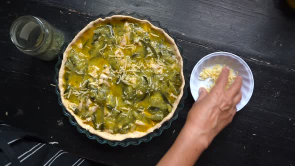 Woman's Hand Sprinkling Grated Cheese On Top Of Zucchini Pie Before Baking. overhead shot alt