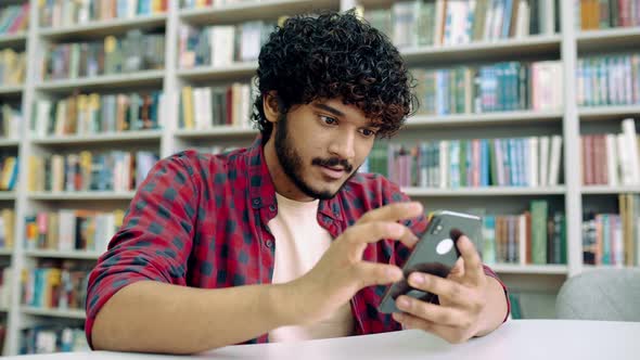 Happy Indian or Arabian Millennial Guy Freelancer or Student Using His Smartphone Chatting with alt