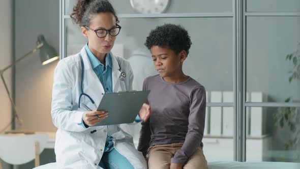 African American Kid Talking with Female Doctor on Consultation in Clinic alt