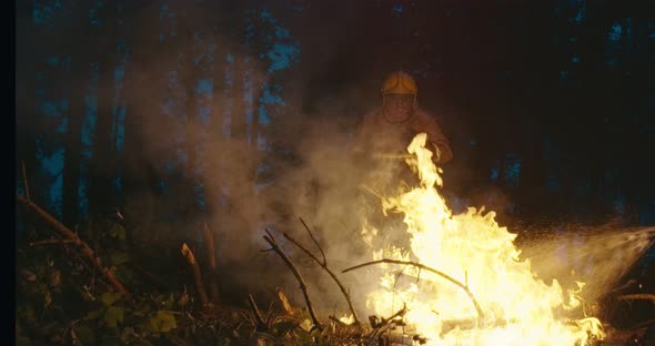 Fire Fighter with Safety Equipment and Axe Extinguishing Fire in Forest at Night alt