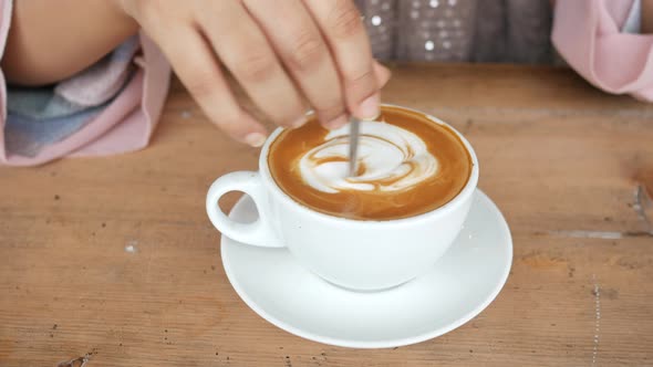 Person Hand Stirring a Cup of Coffee with Spoon alt