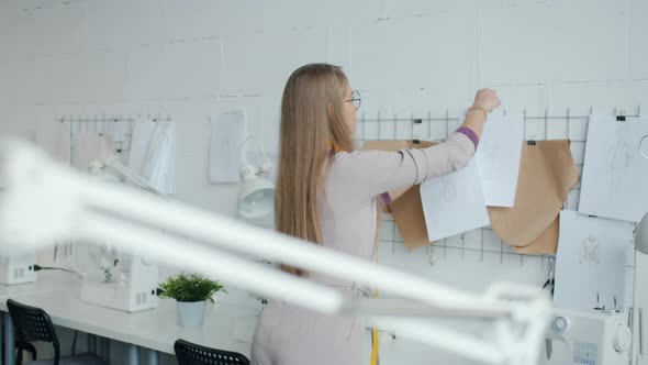 Beautiful Young Woman Tailor Hanging Sketches and Thinking About New Collection in Modern Workshop alt