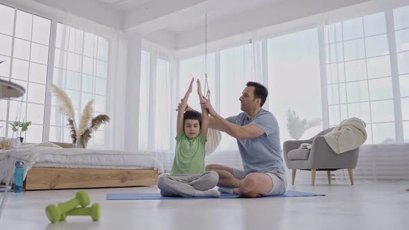 Caring Dad Helping Son to Keep Yoga Pose Indoors alt
