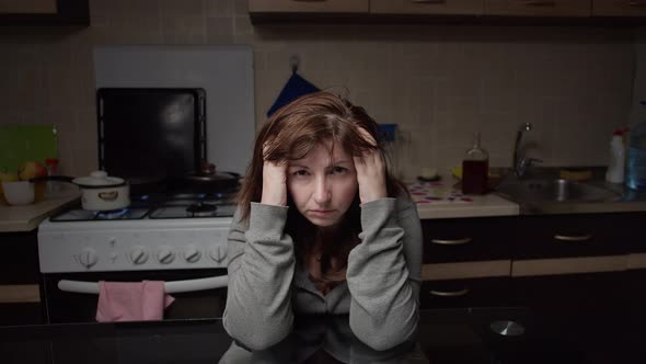 Sad Tired Woman Sitting in the Kitchen at Home and Looking at the Camera