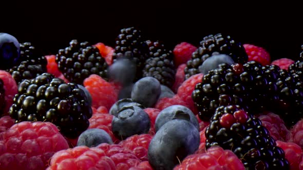 Fruits falling down. Plate full of blueberries, blackberries and raspberries on a black background