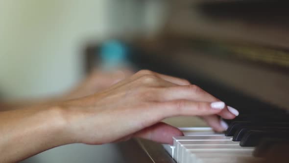 The hands of a young woman take over the keys while playing the piano.