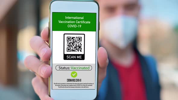 Man in medical mask showing an International Vaccination Certificate COVID-19 QR code on smartphone alt