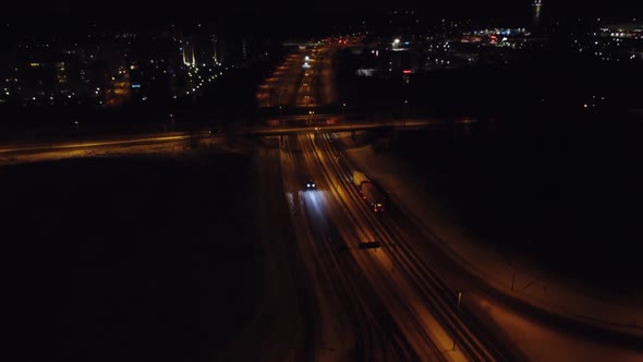 Retreating night aerial tilts up to reveal light winter city traffic alt