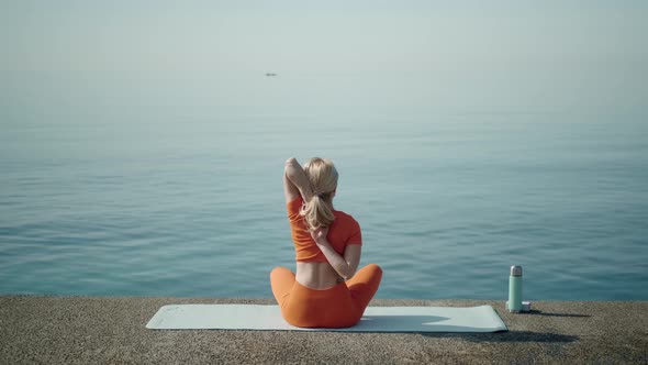 A Woman Sits in a Lotus Position Near the Sea Joins Hands Behind Back