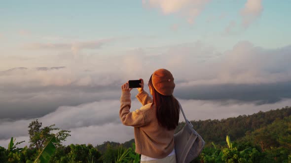 Young woman traveler taking photo with smart phone at sea of mist