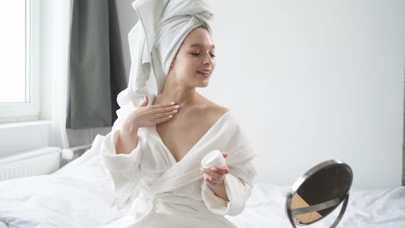 Beautiful Female in Towel and Bathrobe Applying Cream on Body in Morning