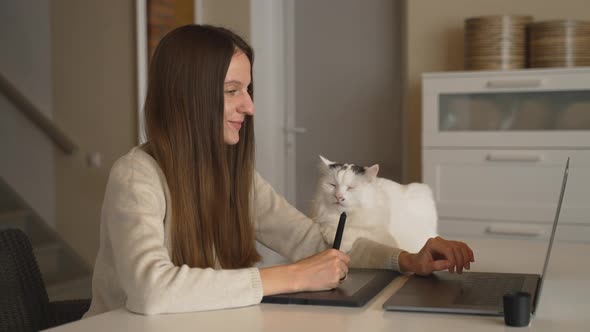 Female Freelance Designer at Home Draws on Pen Tablet and Pets White Cat on Desk