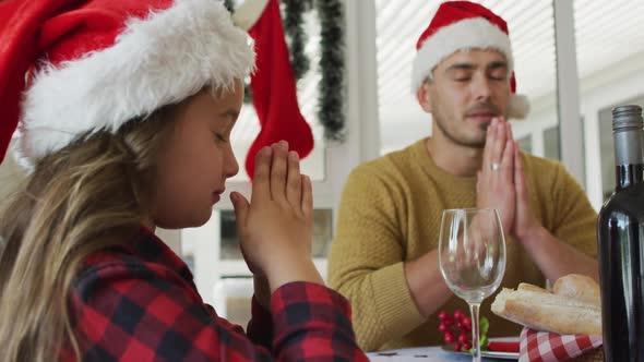 Focused caucasian daughter and father praying together before christmas dinner alt