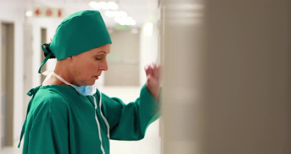 Tensed female surgeon leaning on wall in corridor alt