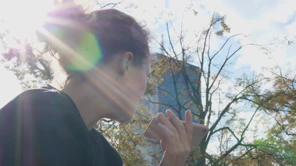 Woman Recording Voice Message on the Smartphone on a Sunny Day at the Park alt