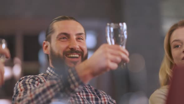 Joyful Man Clinking Beer Glasses with Friends Sitting in Bar Indoors alt